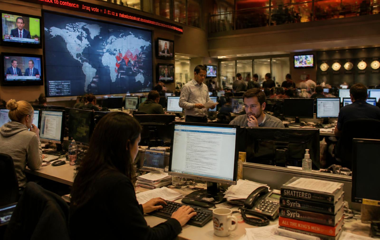 Journalists working in a global newsroom in front of a large world map display